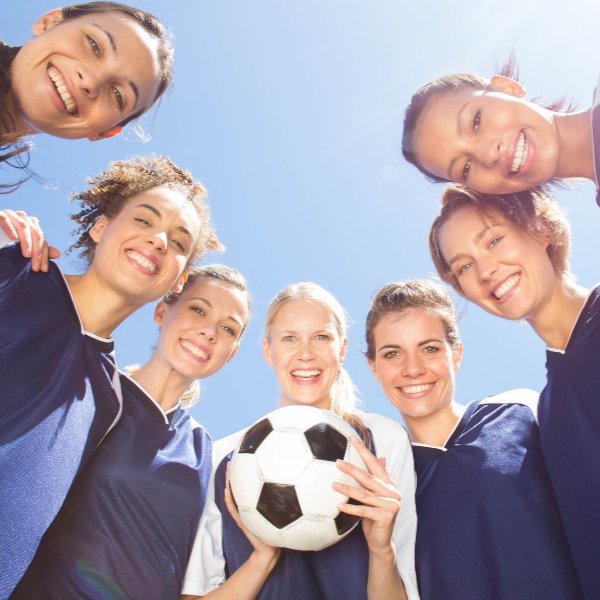 Group of people in sports uniforms holding a soccer ball against a clear blue sky.