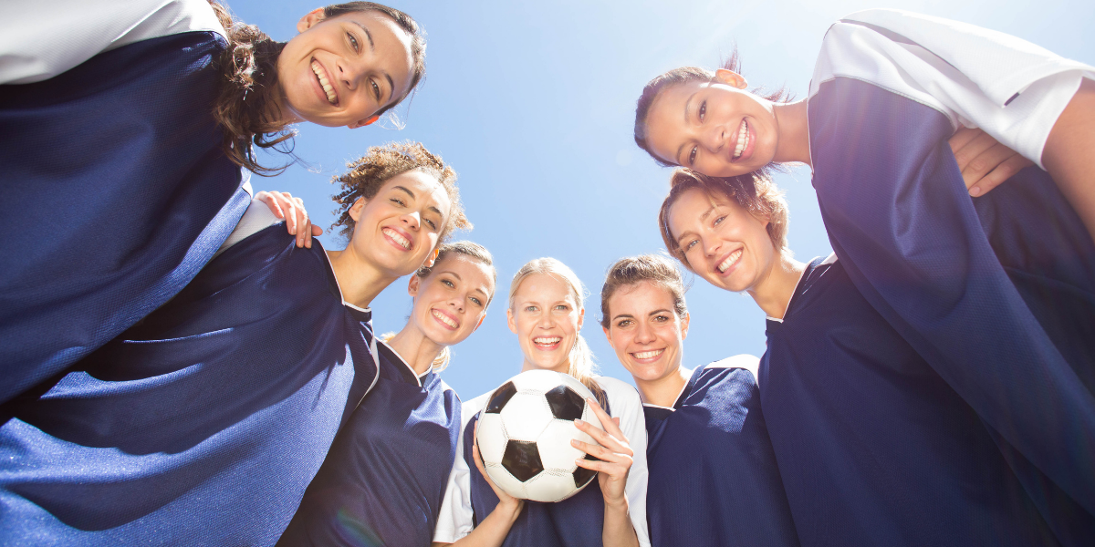 Group of soccer players in blue uniforms with a soccer ball against a clear blue sky.