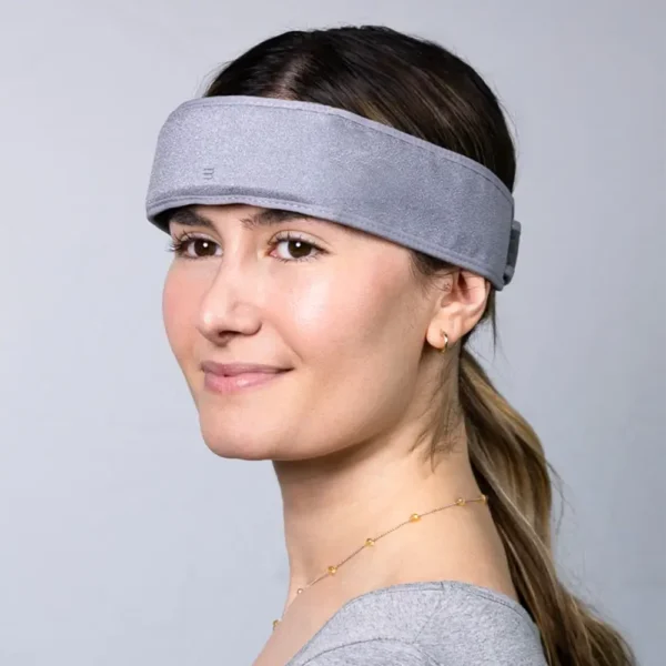 A photo of a smiling blond woman in a gray shirt, facing to the front left, wearing the SONU band which is a gray band that stretches around her head like a headband